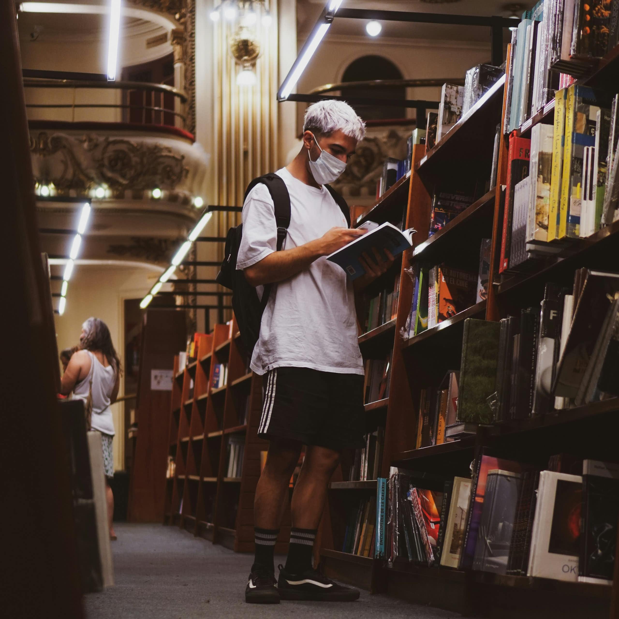 A man wearing a mask reading a book in a library