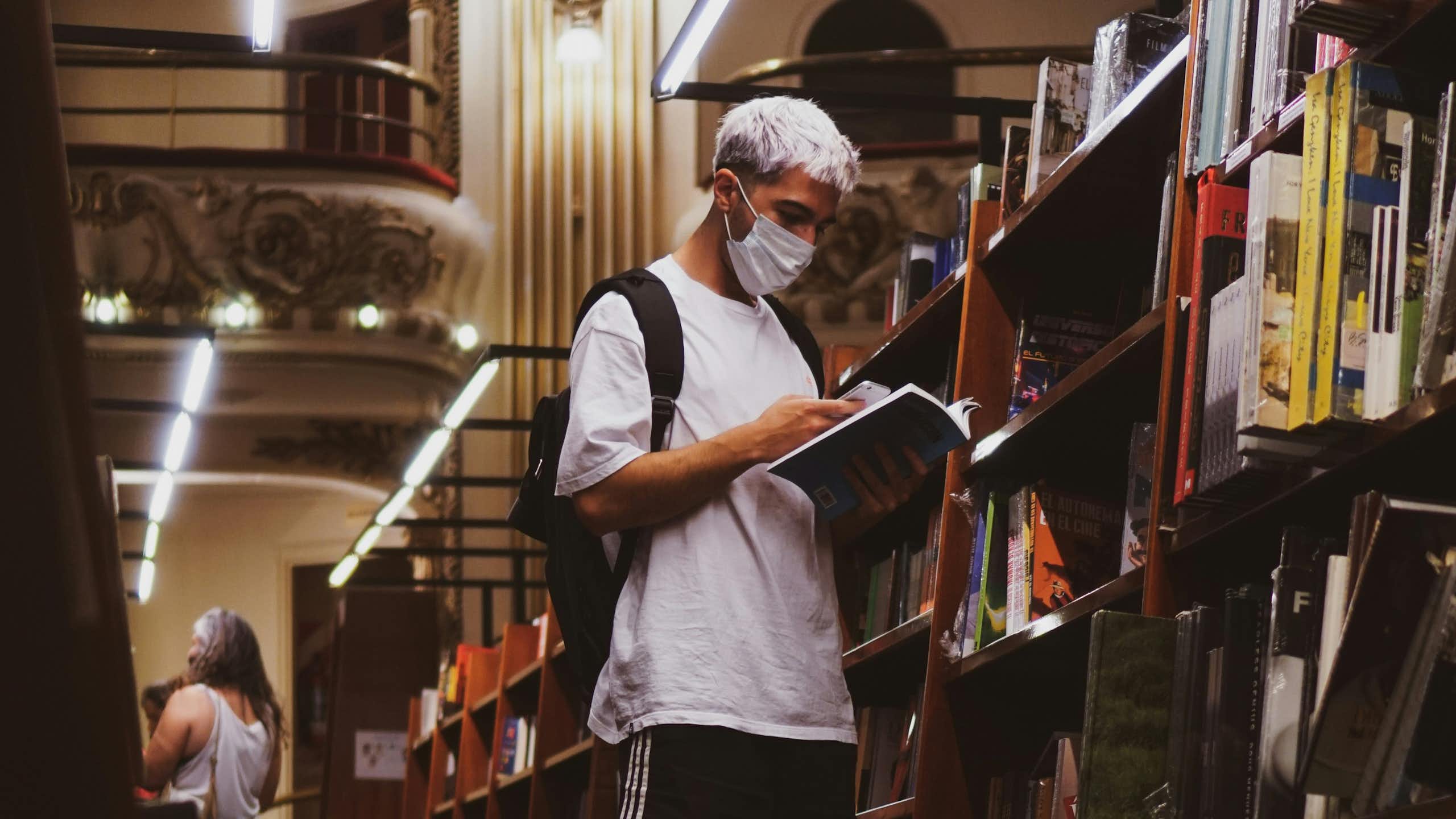 A man wearing a mask reading a book in a library