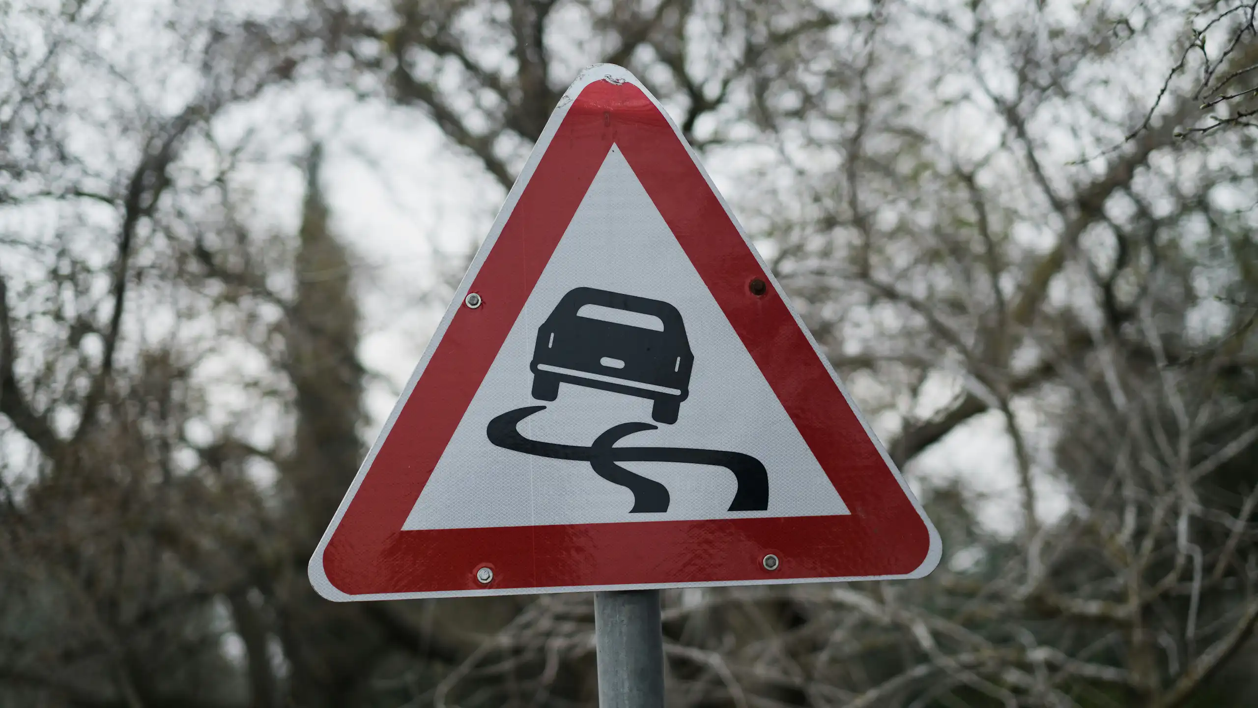 A triangular road sign with an icon of a skidding car