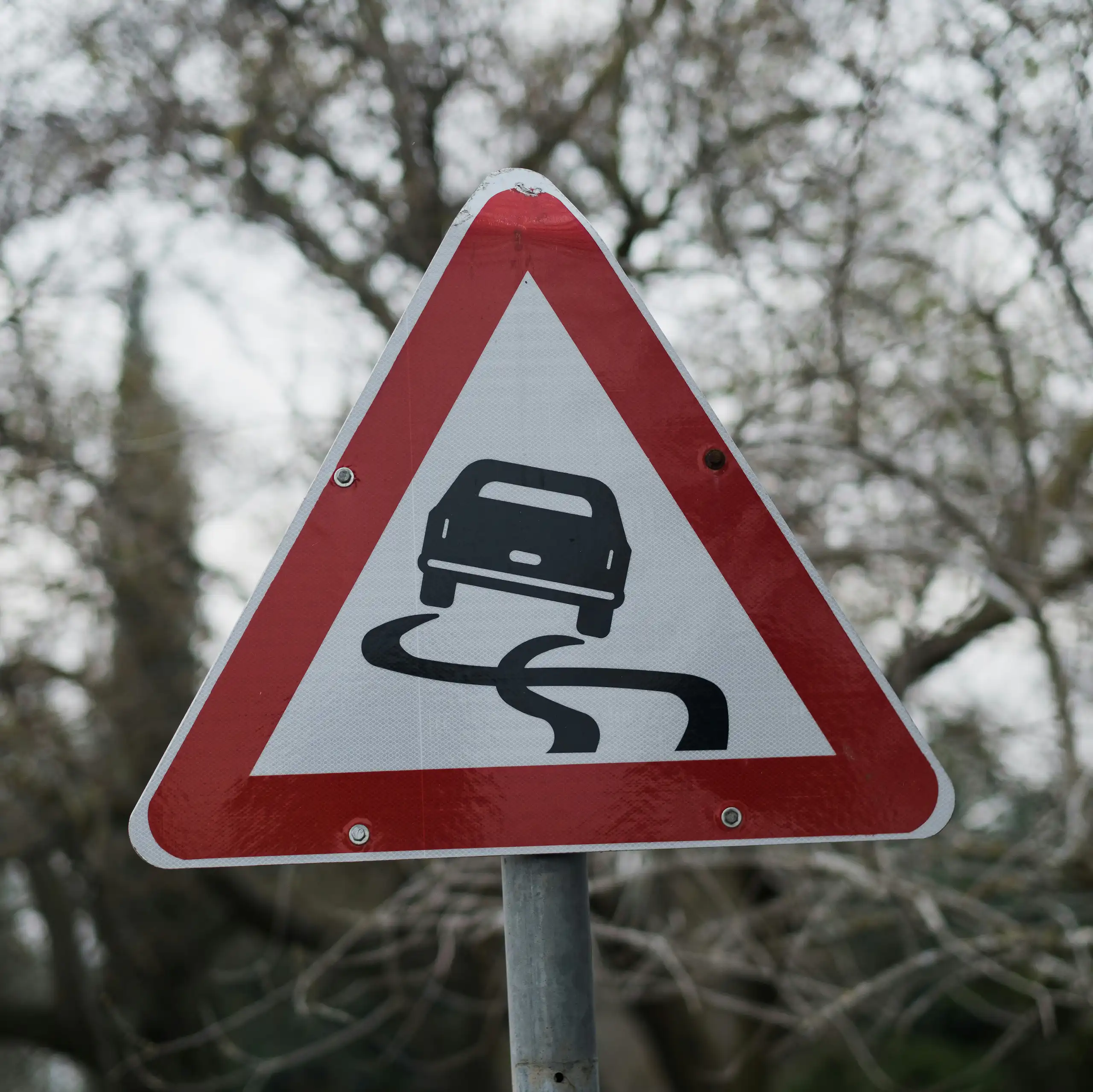 A triangular road sign with an icon of a skidding car
