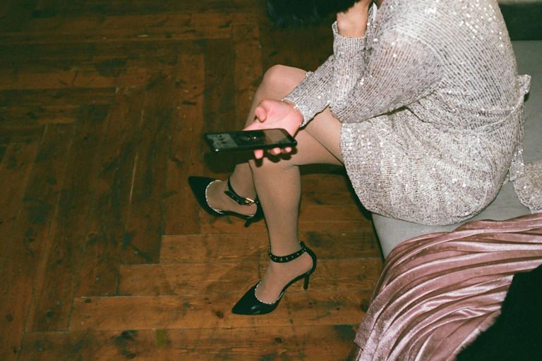 a woman in a sequinned dress and heels, holding a mobile phone