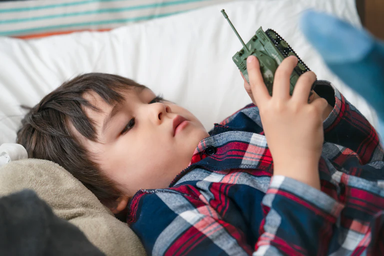 A boy laying in bed holding a toy tank