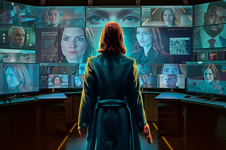 Holliday Granger with her back to us, looking at a large screen full of images of faces