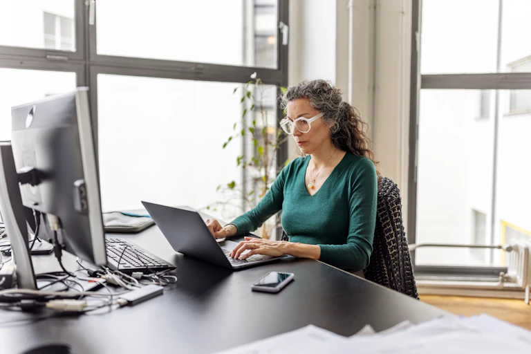 A woman works at a laptop in an office.