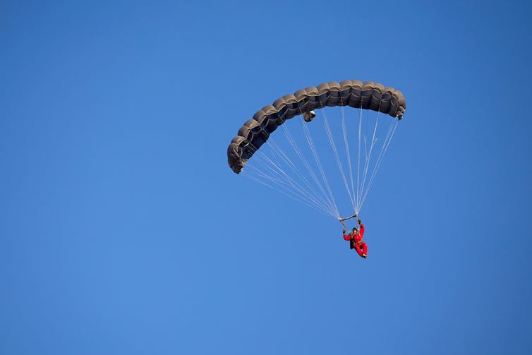 A pilot floating earthward, parachute deployed.