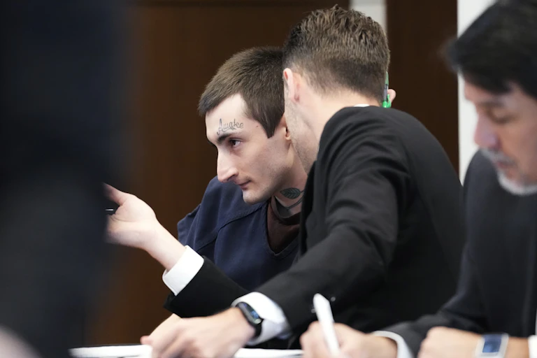 A man leans over an points while talking to a tattooed man who is staring straight ahead in a courtroom.