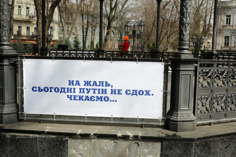 An outdoor rotunda with iron railings supports a white sign with blue text in Ukrainian.