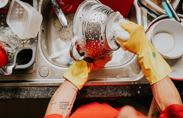 Una persona con guantes de goma amarillos lava platos.