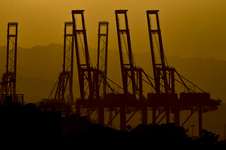 The silhouettes of container cranes against a sunset