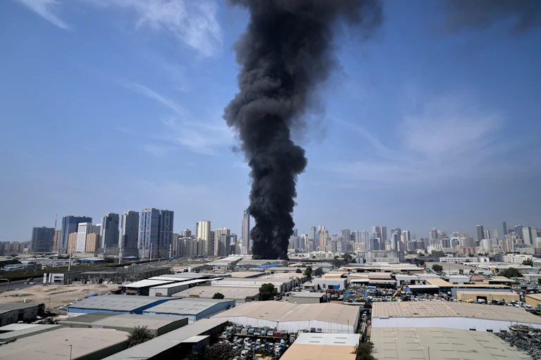 A large black plume of smoke spewing from a warehouse in an industrial area.
