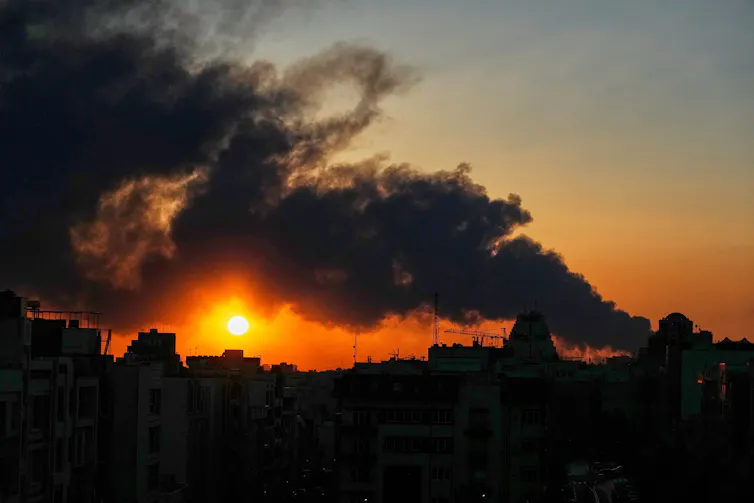 A setting sun behind a plume of black smoke rising in the sky.