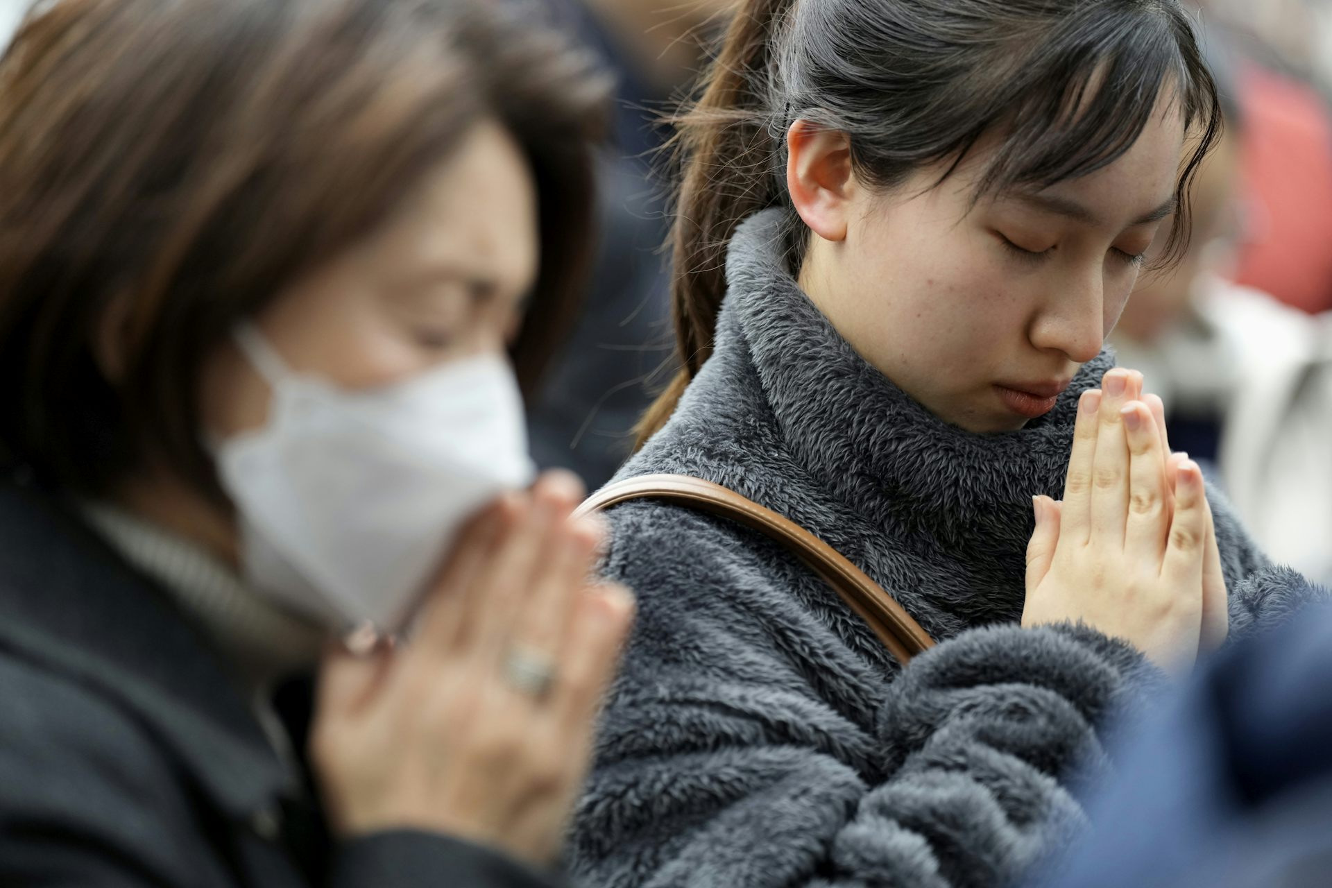 Las mujeres de Asia oriental permanecen con las manos entrelazadas y la cabeza inclinada en oración.