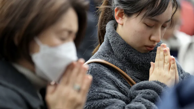 east asian women stand with their hands pressed together and bowing their heads in prayer