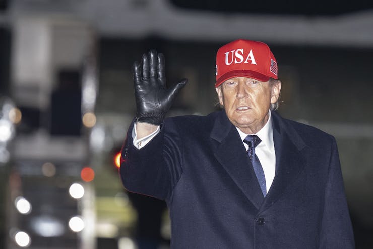 An older man in a blue coat and red hat with 'USA' written on it waves.