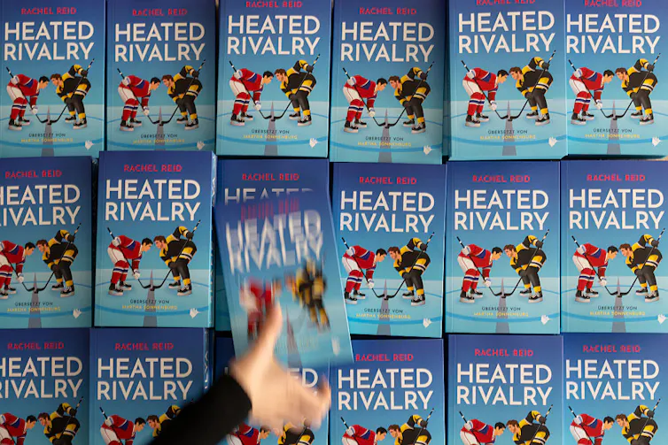 A blurry hand-in-motion removes a book from a display featuring the same title, 'Heated Rivalry.'