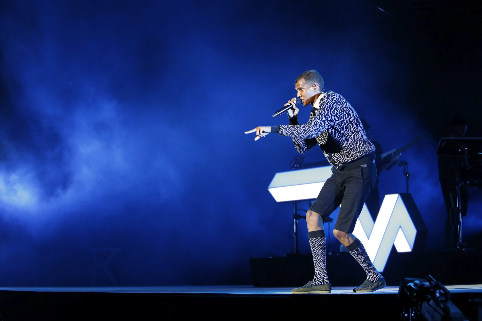 Un músico en el escenario sostiene un micrófono y canta.