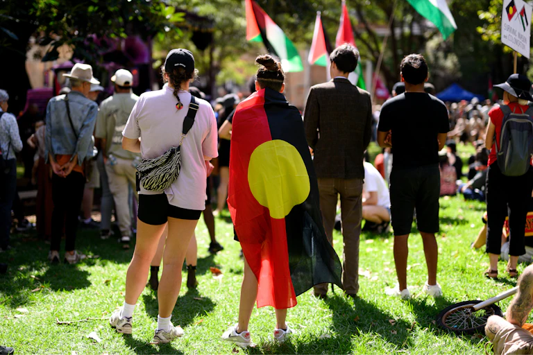 The backs of a group of women and man, with the central woman wearing an Aboriginal flag around her shoulders
