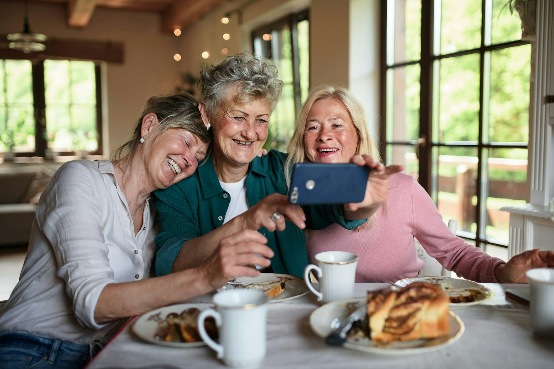 Three women take a selfie together while sitting together for a meal at a restaurant.
