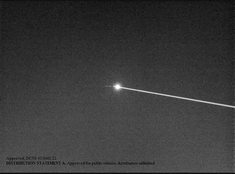 Black and white photo of a laser beam hitting a small object