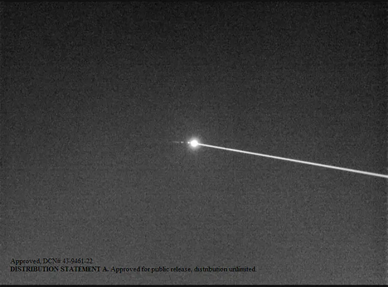 Black and white photo of a laser beam hitting a small object