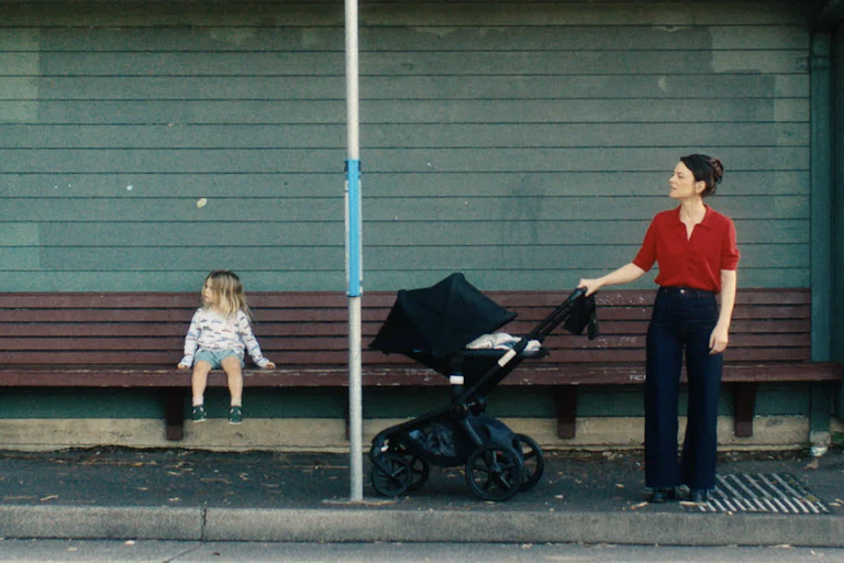 Film still: a mother and a toddler at a bus stop.