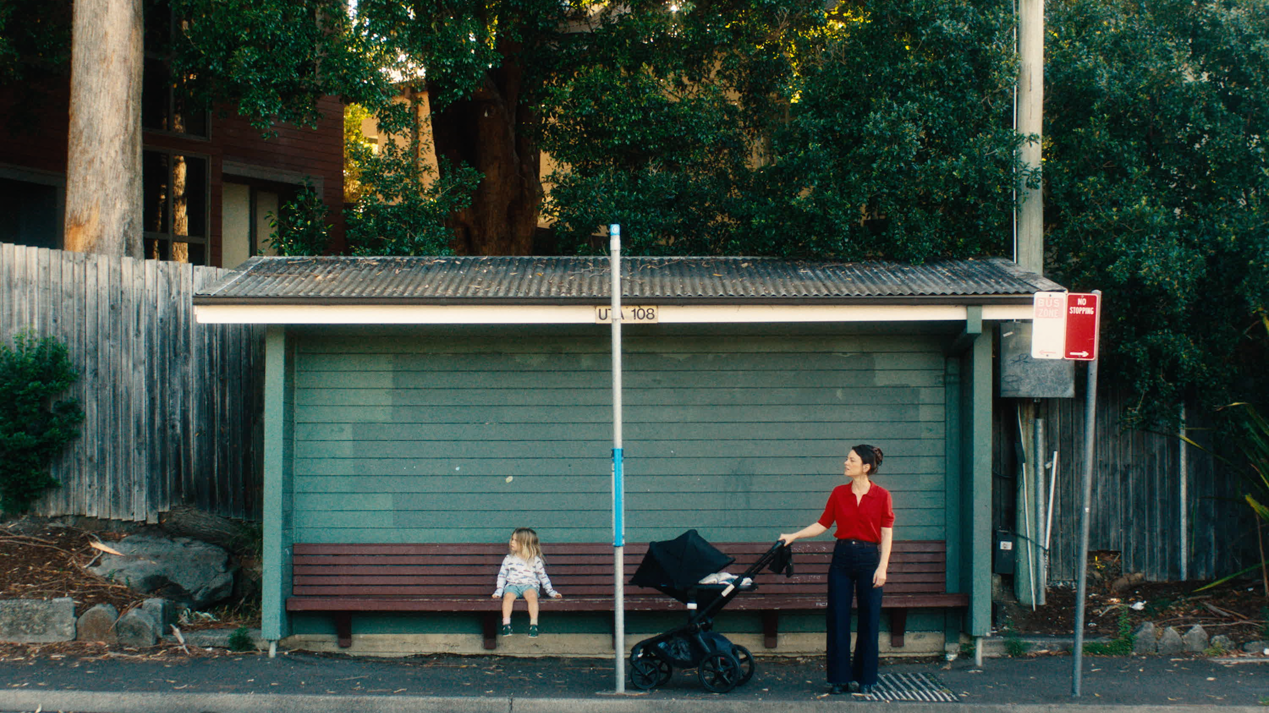 Film still: a mother and a toddler at a bus stop.