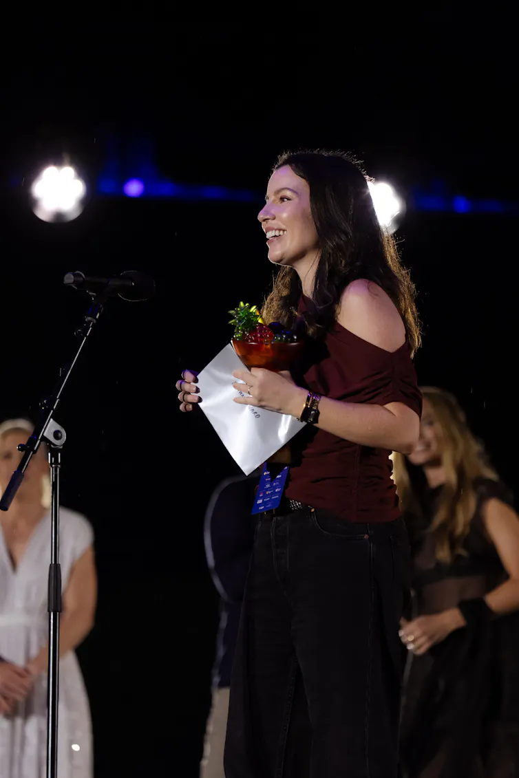 A woman stands at a microphone with a pineapple award.