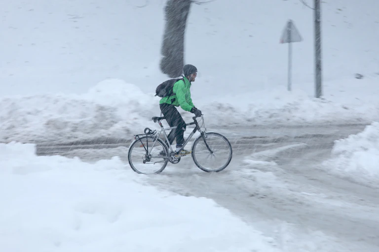 A cyclist on a very snowy road at a crossroads in Stockholm, Sweden.