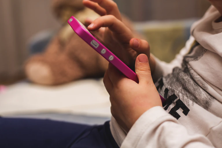 Child's hands holding pink mobile phone