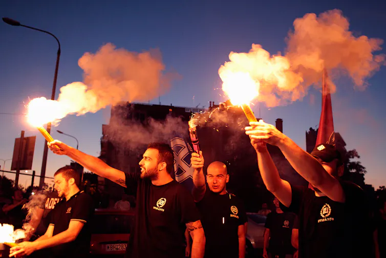 young greek men holding flares in support of the far-right golden dawn party.