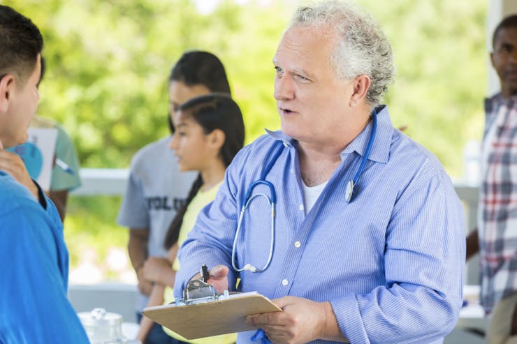 Senior public health doctor talking to patient at temporary free outdoor clinic