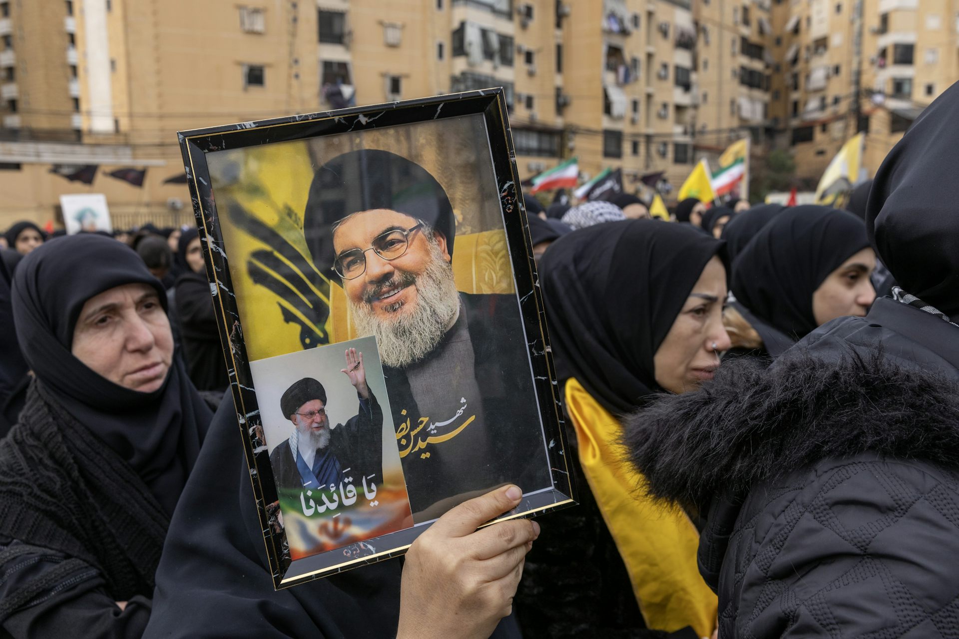 Women in black Muslim dress hold a picture of a man with a beard.