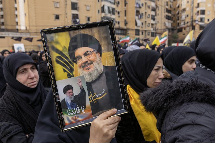 Women in black Muslim dress hold a picture of a man with a beard.