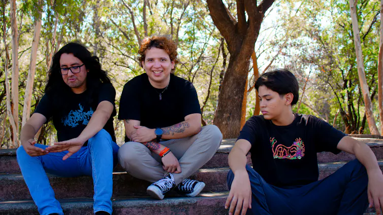 Three young people sitting outdoors, side by side.
