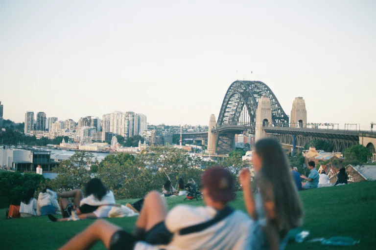 People sit on the grass, overlooking the Sydney Harbour Bridge