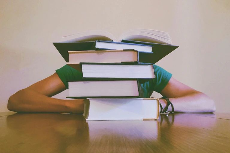 A person behind a stack of large books.