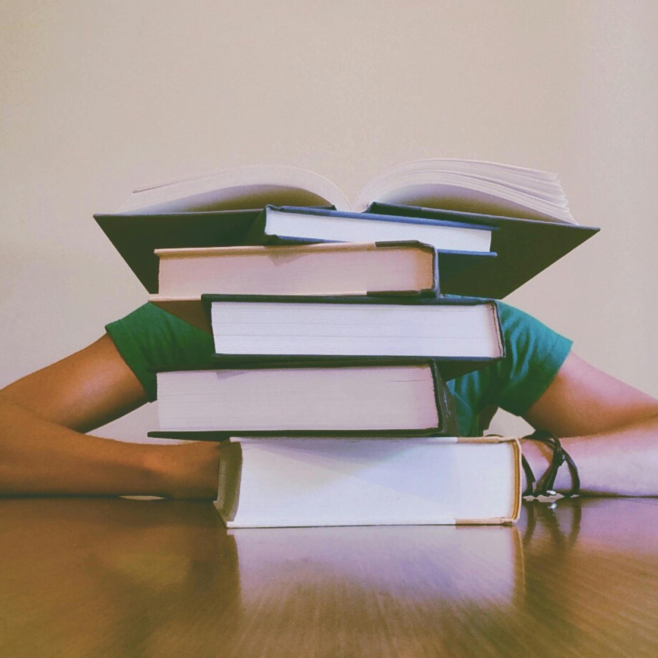 A person behind a stack of large books.