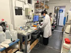 a woman wearing a white lab coat stands in front of a table in a lab