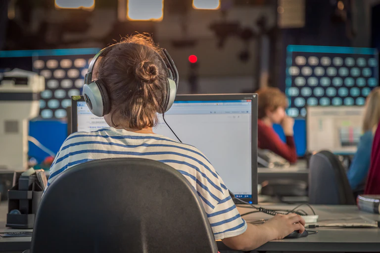 View from behind of a young woman working on a computer in a newsroom
