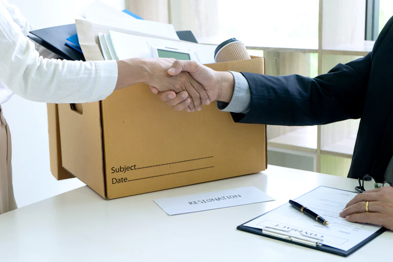 Personne partant de son travail avec un carton serrant la main de son patron.