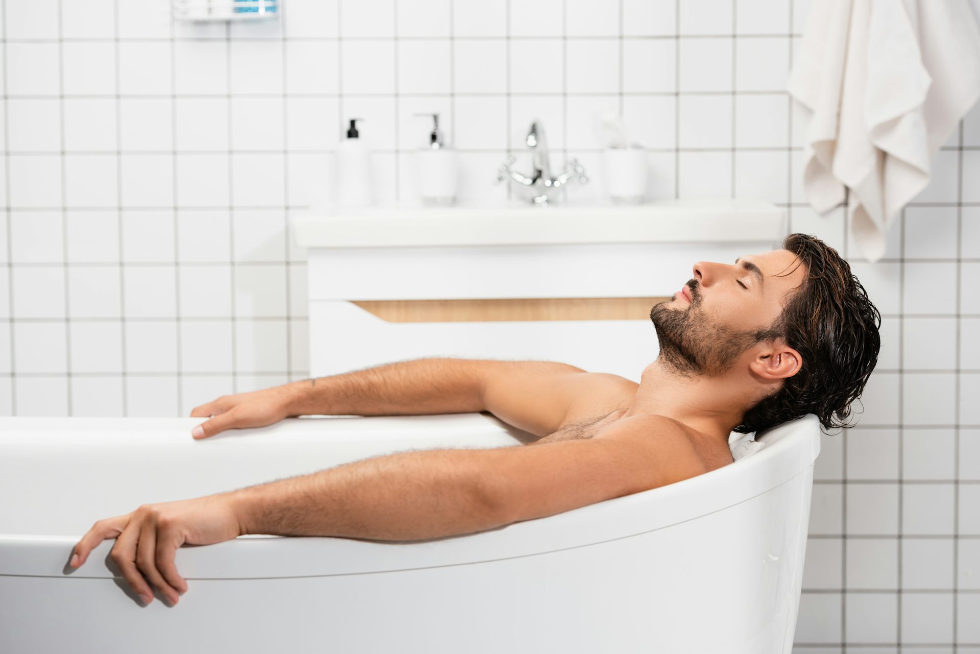 Bearded man leaning back in a hot bath with his eyes closed.