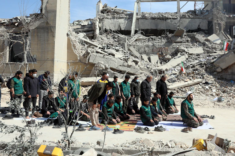A group of men kneeling next to a damaged building
