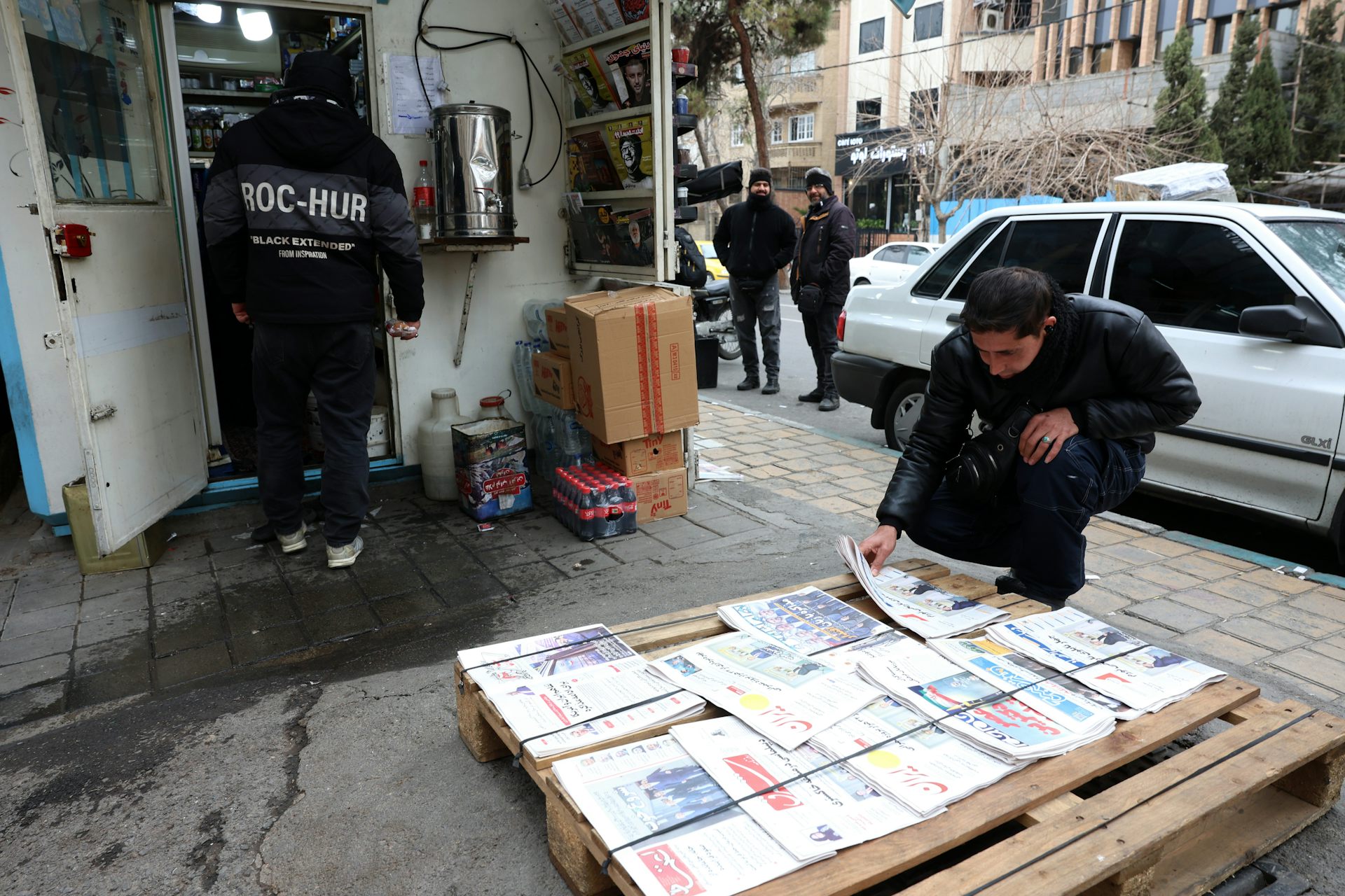 A man looks at newspapers laid out on a pallet on a public street