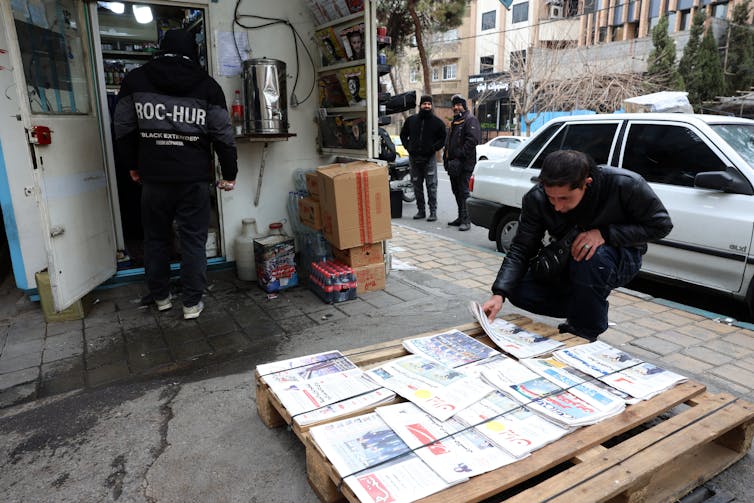 A man looks at newspapers laid out on a pallet on a public street