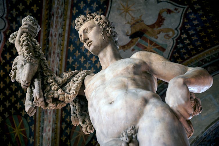 A marble statue of a naked man holding up the head and fleece of a ram.