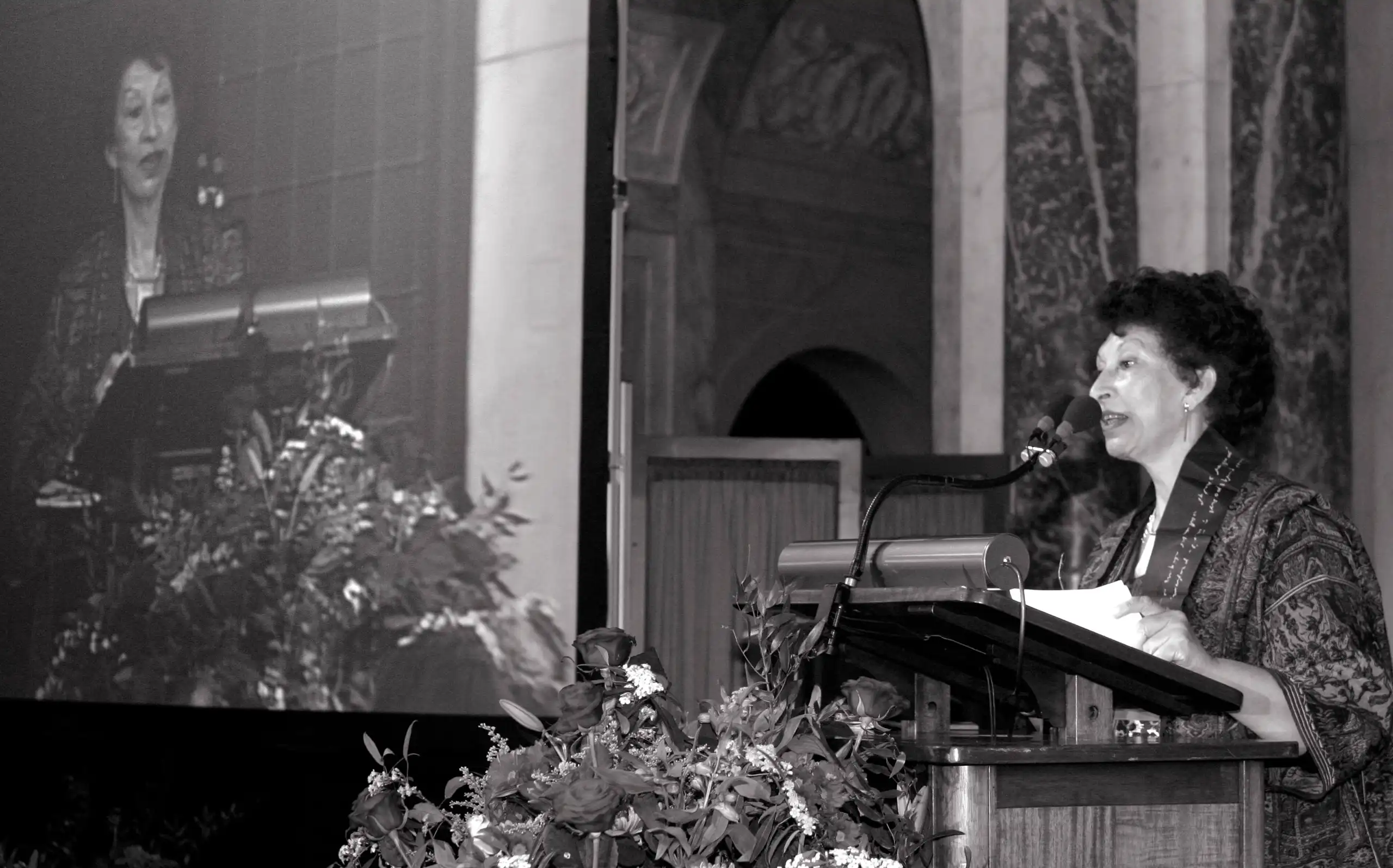 Foto en blanco y negro de una mujer dando un discurso en un atril.