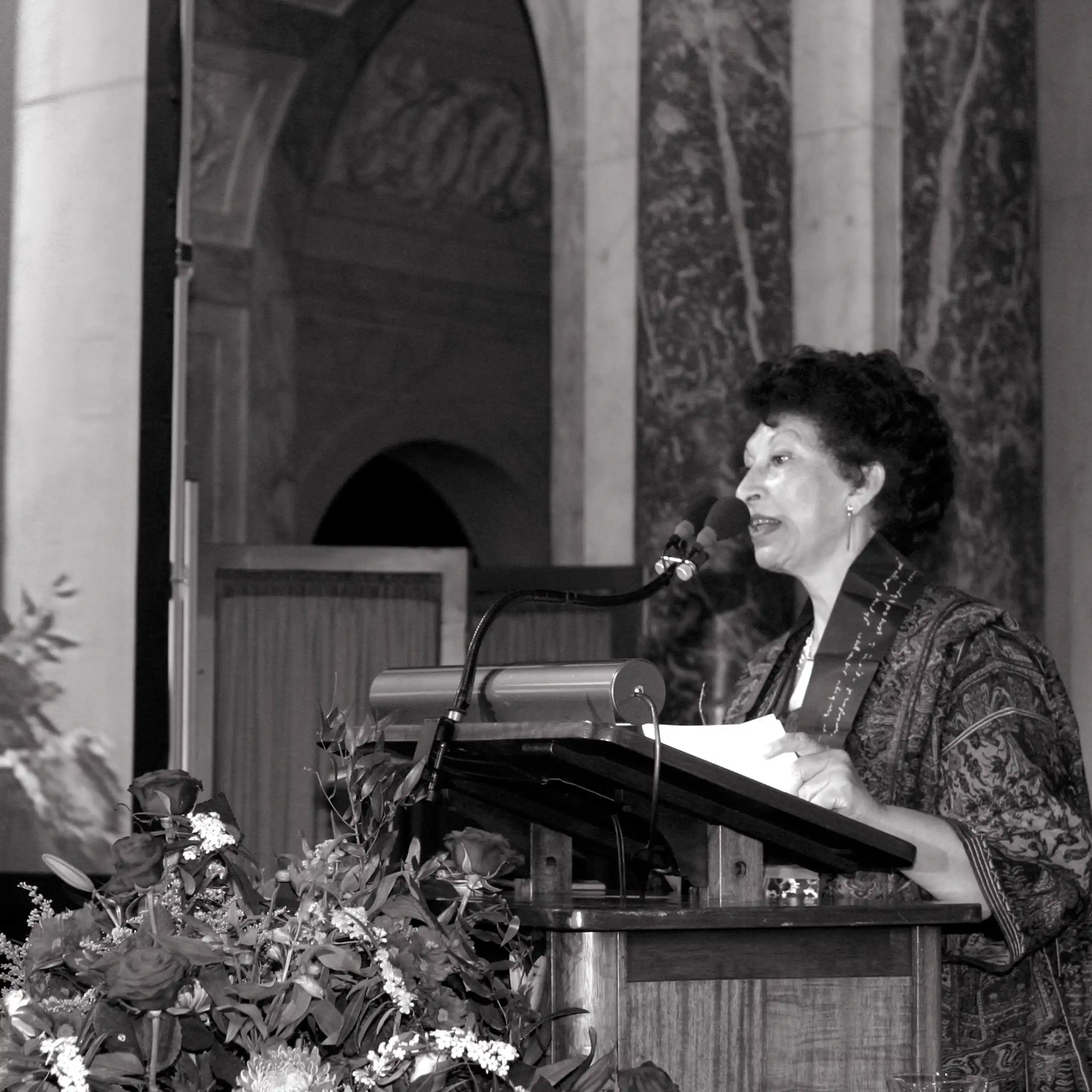 Foto en blanco y negro de una mujer dando un discurso en un atril.