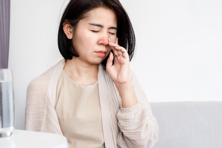 A woman touches her blocked nose with her hand.