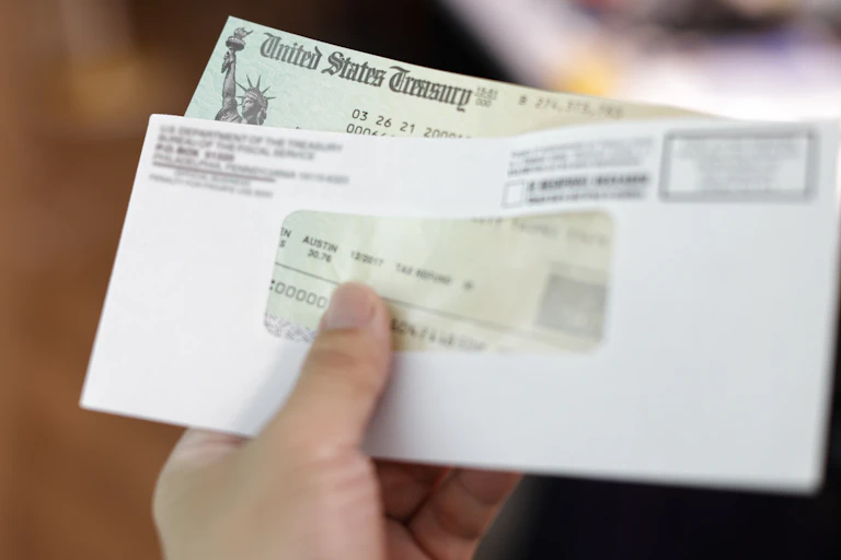 A hand holds an envelope with a check from the US treasury inside.