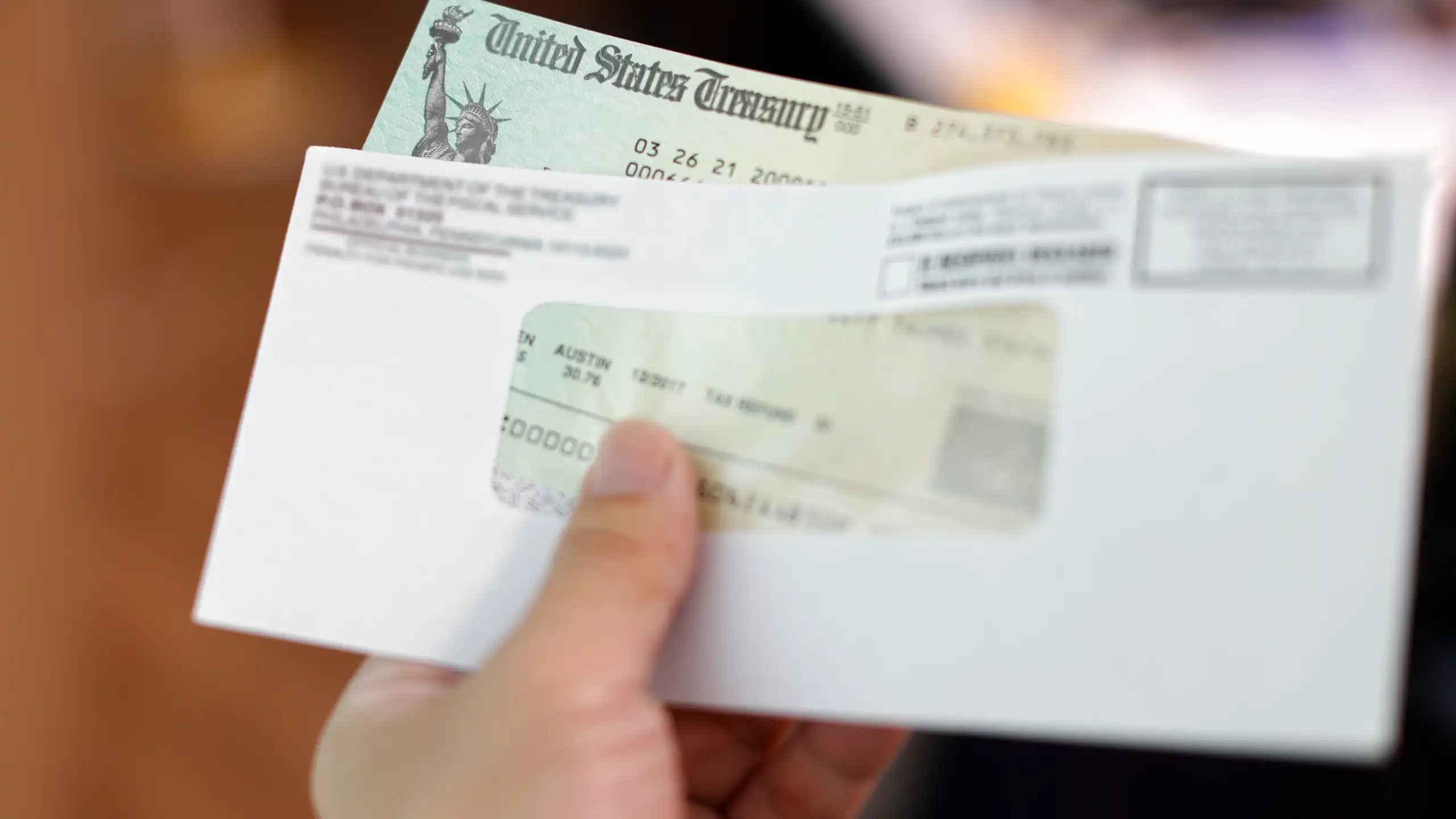 A hand holds an envelope with a check from the US treasury inside.